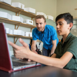 A teacher helps a student at a laptop